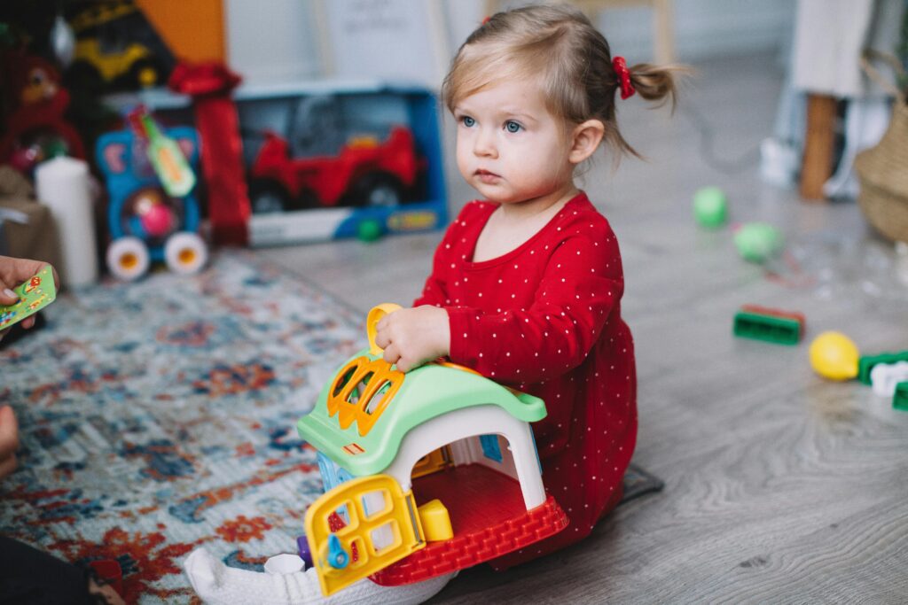 Adorable toddler in red outfit playing with toy house indoors. Perfect for playtime and childhood themes.