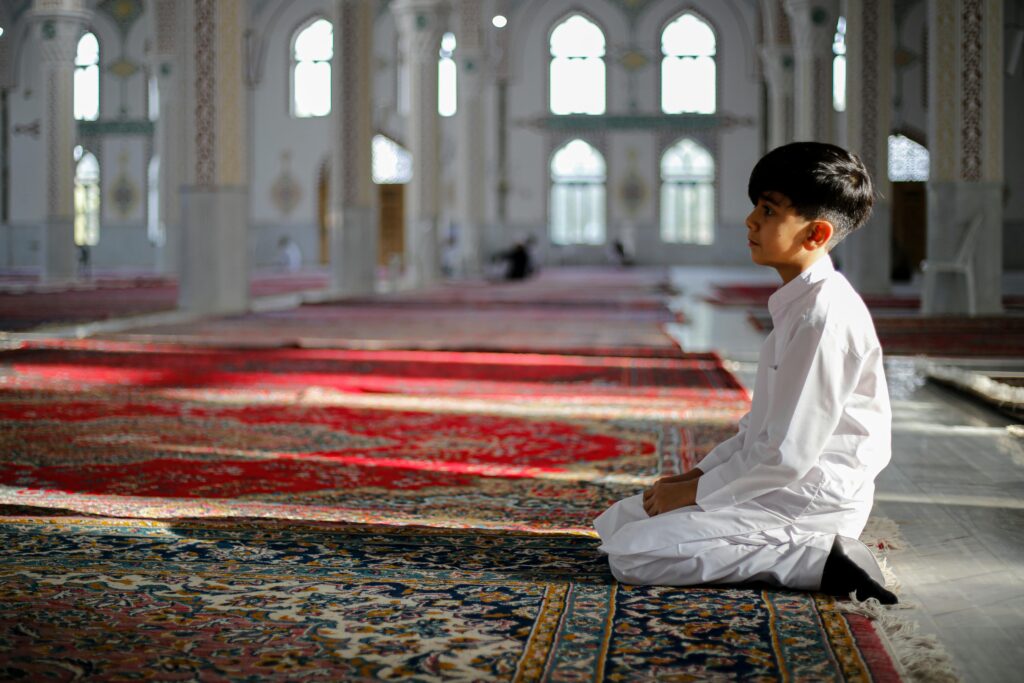 A young boy kneels in prayer inside a mosque in Khaf, Iran, showcasing serenity and spirituality.