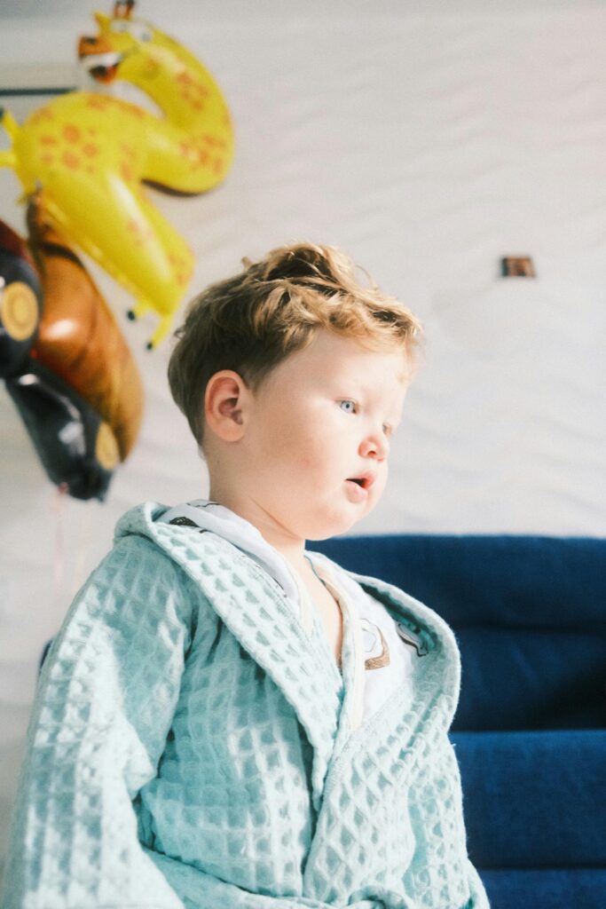 A young child in a blue robe indoors, surrounded by colorful balloons, brings a sense of joy and innocence.