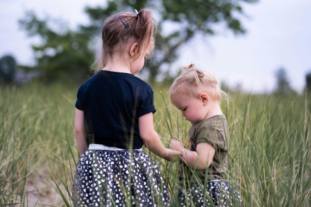 Two young sisters explore a grassy field during a warm summer day, capturing childhood joy.
