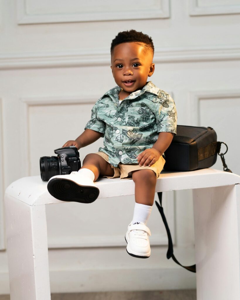 Cute black baby boy sitting on a stool in a studio setting with a camera.