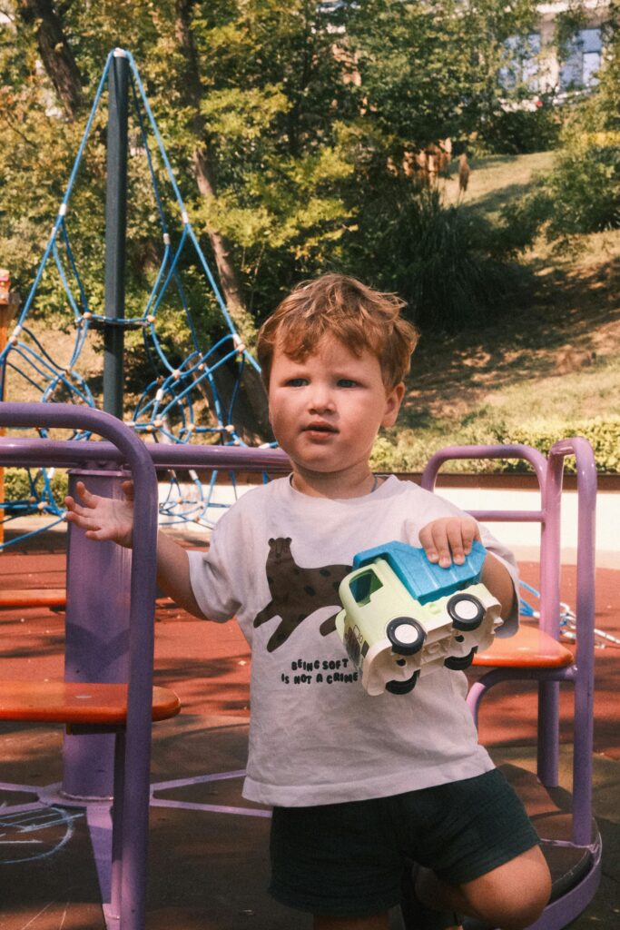 Cute child playing with a toy car in the sunny park, wearing a fun animal t-shirt, embodies summer joy.