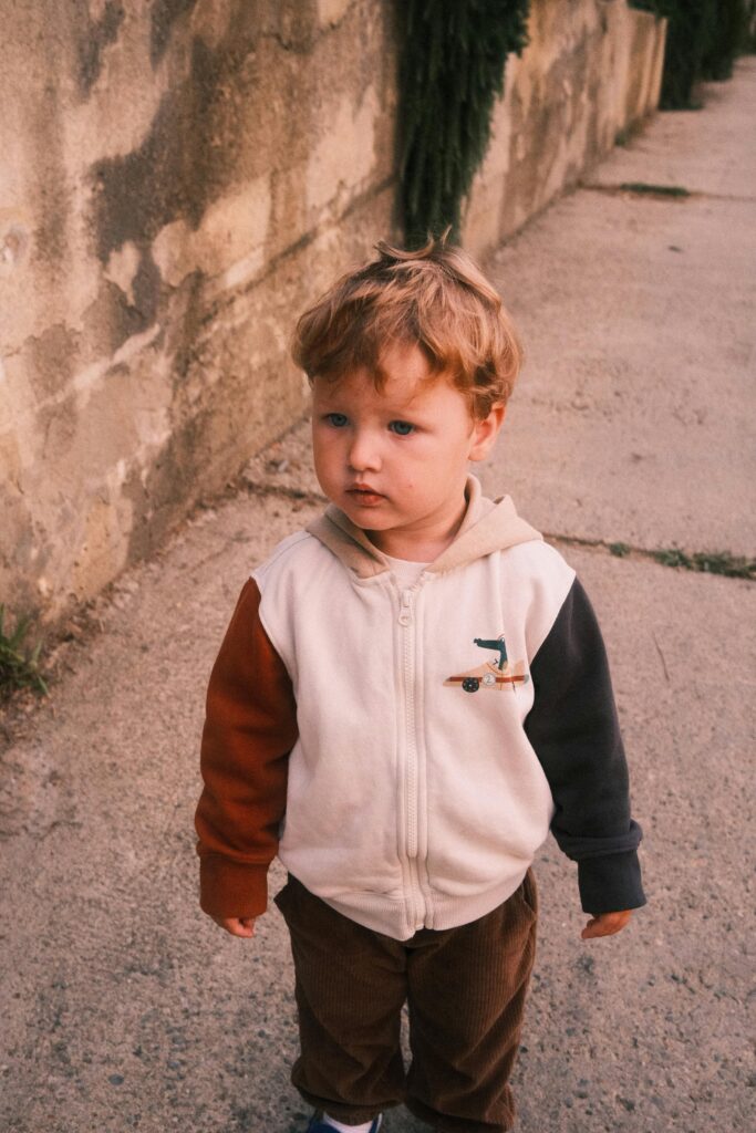 Adorable young boy in a color-blocked hoodie standing outdoors with a curious expression.