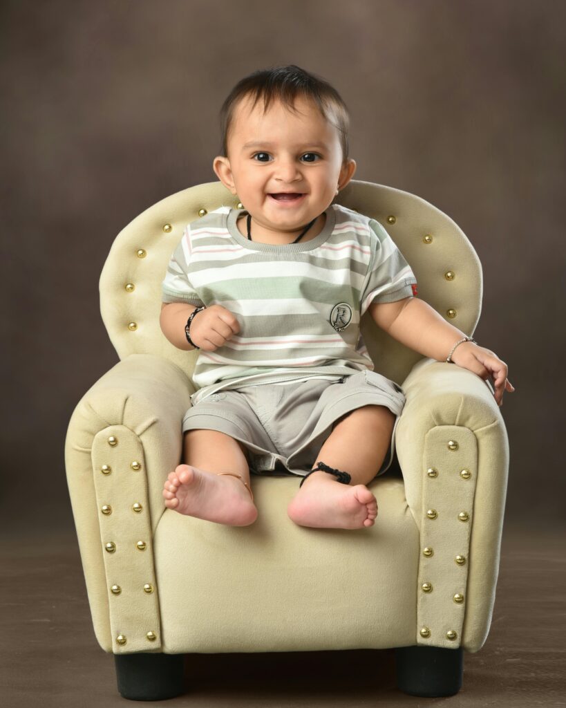 Adorable South Asian baby boy smiling in a plush chair indoors.