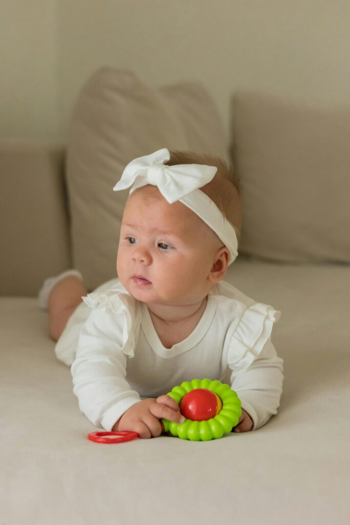 Adorable baby girl in white with a colorful toy on a cozy sofa. Perfect for parenting themes.